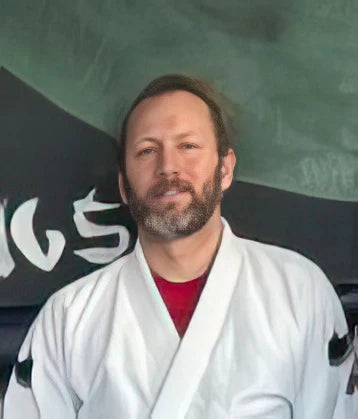 Justin Barker, a Brazilian Jiu-Jitsu instructor, standing in front of the gym chalkboard